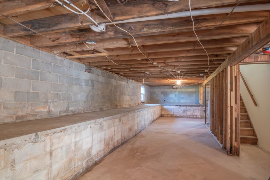 Basement Waterproofing in Fort Lee, NJ — Empty basement with exposed wooden beams, concrete walls and stairs.