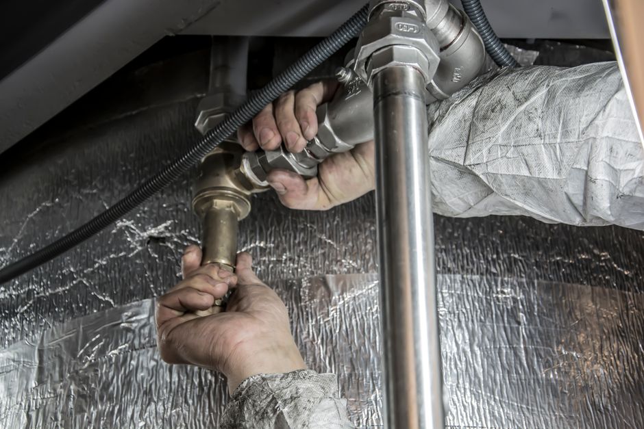 Sump Pump Installation & Replacement in Fort Lee, NJ — Close-up of a plumber's hands installing steel pipes indoors, showcasing skilled manual work.